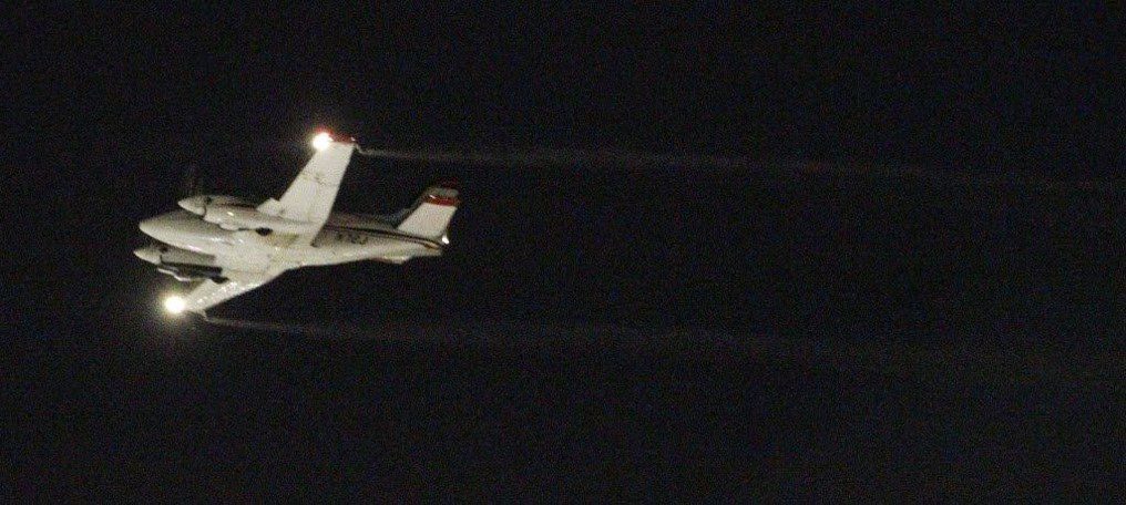 A drone airplane flying at night, distributing pesticide products over a wide area.
