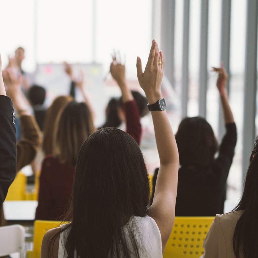 people in a classroom all raising their hands